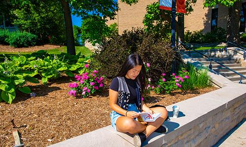 a 博天堂官方入口登陆登录 student sitting on a ledge reading a book.